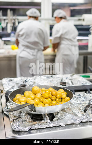 Kleine Kartoffeln auf Silber pan mit zwei Küche Arbeiter mit Schürzen als Hintergrund Stockfoto