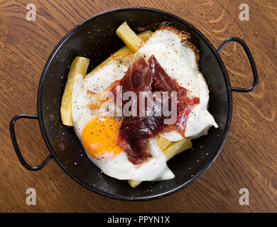 Blick von oben auf die traditionelle spanische Spiegeleier mit Jabugo Schinken auf Pfanne bei Holz- Oberfläche serviert. Stockfoto