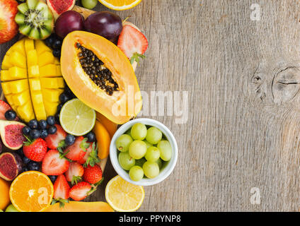 Ansicht von oben von bunten Früchte, Erdbeeren, Blaubeeren, Mango, Orange, Grapefruit, Bananen, Papaya apple, Trauben, Kiwis auf der grauen Holz Hintergrund, Stockfoto