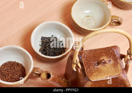 Tassen und Keramik Teekanne mit grüner Tee Blätter und rooibos. Es steht auf einem Holztisch. Stockfoto