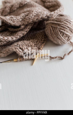 Beige stricken Wolle und Stricknadeln auf weißem Holz- Hintergrund. Stricken als Hobby. Zubehör für Stricken. Stockfoto
