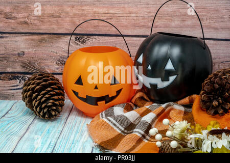 Gemütliche Halloween Herbst Konzept Hintergrund mit Kürbis jackolantern Eimer, orange plaid Decke, Tannenzapfen und Blumen auf Holz Hintergrund Stockfoto
