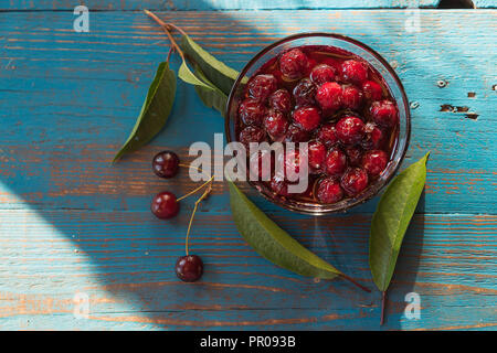 Cherry jam in Glasschale, über alte blaue Holztisch, Tageslicht, flach. Stockfoto