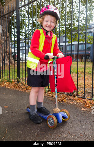 4 Jahre altes Kind auf Roller / Mädchen in Ihrem Hi-vis/hohe Sichtbarkeit Weste, rollerfahren von der Schule nach Hause Rezeption klasse. UK. (102) Stockfoto