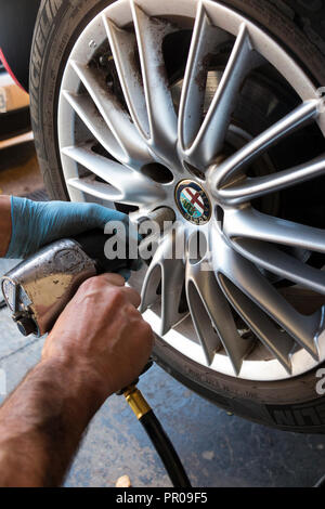 Reifen Monteur/Mechaniker Lockern/Lösen/lockert Schrauben auf ein Auto, das mit einer alten umgekommen Reifen, so dass es für einen neuen Reifen geändert werden können. (102) Stockfoto