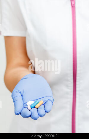 Hand der Ärztin in blau Handschuh mit Haufen Pillen der anderen Farbe mit Fokus auf Pillen Stockfoto