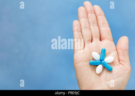 Nahaufnahme einer Hand, die blaue und weiße Pillen in der Form wie Blume. Pillen auf Frau hand Stockfoto