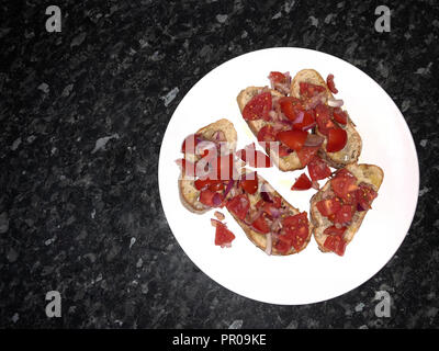 Spanische Tapas weiße Platte mit geröstetem Brot, Olivenöl, gehackte Tomaten und Zwiebeln, auf schwarzem Marmor Zähler nach oben. Stockfoto