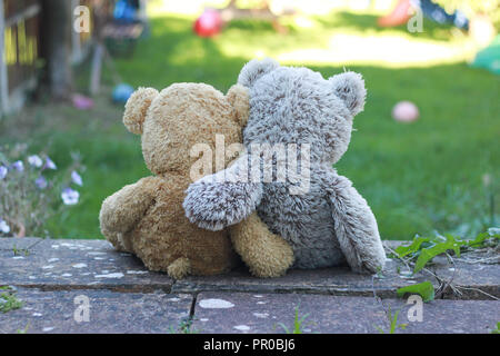 Zurück Blick auf zwei Teddybären mit Ihren Armen herum und saß auf einem Schritt, mit Blick auf den Garten. Stockfoto