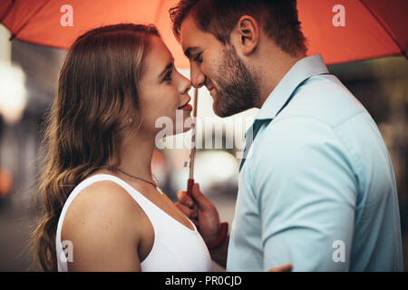 In der Nähe von ein paar Stand unter einem Sonnenschirm Ihre Nase berühren. Mann und Frau in der Liebe gemeinsam einen Regenschirm bei Regen im Freien Holding Stockfoto