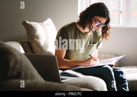 Junge Menschen studieren für Prüfungen auf der Couch zu Hause sitzen. Student Studium zu Hause mit Bücher und Laptop. Stockfoto