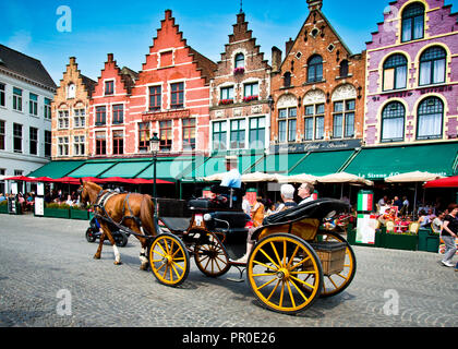 Touristen, die auf eine Stadttour in einer Pferdekutsche durch alte Gebäude genommen werden, jetzt Cafés und Restaurants mit verzierten Giebeln in der historischen Brügge, Stockfoto