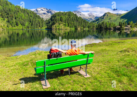 Wanderer mit Rucksack entspannt auf einer Bank, See Cavloc, Forno Tal, Malojapass, Engadin, Graubünden, Schweiz, Europa Stockfoto