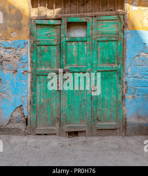 Geschlossen grünes Holz- Grunge verwitterten aufgegeben Tür auf schmutzige Wand in Gelb und Blau lackiert Stockfoto