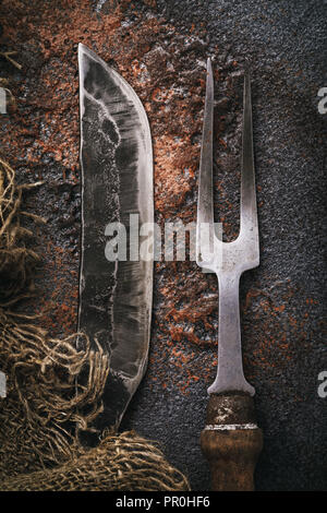 Messer und Gabel für Fleisch auf einem rostigen Tabelle. Blick von oben auf die vintage Küchengeräte Stockfoto
