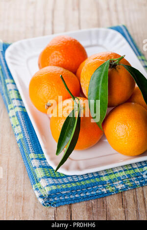 Mandarinen mit Blättern in der Platte auf hölzernen Hintergrund Stockfoto