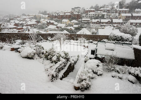 Schnee über einen Garten und die umliegende Stadt Gebäude und deren Dächer. Stockfoto