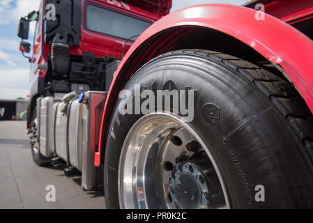 Eine Nahaufnahme Bild eines schwarz glänzend lackiert Reifen, Reifen eines großen roten Prime Mover Lkw geparkt und Stationär Stockfoto