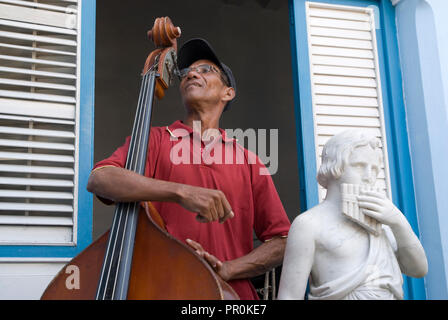 Violoncello Musiker auf seinem Instrument neben einem klassischen Skulptur einer Flöte Spieler in der nördlichen Karibik Kuba Stockfoto