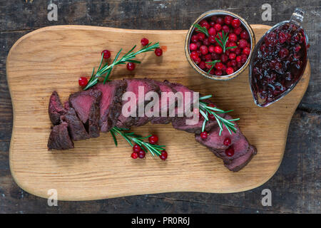 Rehsteak auf Holzbrett mit Preiselbeeren - Draufsicht geschnitten Stockfoto