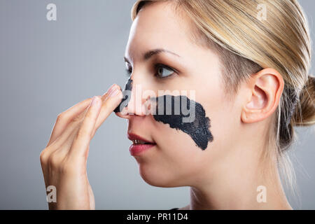 Porträt eines lächelnden jungen Frau Anwendung Aktivkohle Maske auf dem Gesicht Stockfoto