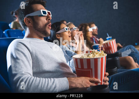 Schockiert multiethnischen Freunde in 3D-Brille mit Popcorn anschauen Film zusammen im Kino Stockfoto