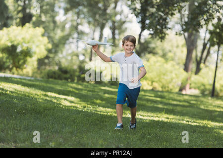 Adorable Happy Boy holding Spielflugzeug und lächelnd an der Kamera in Park Stockfoto