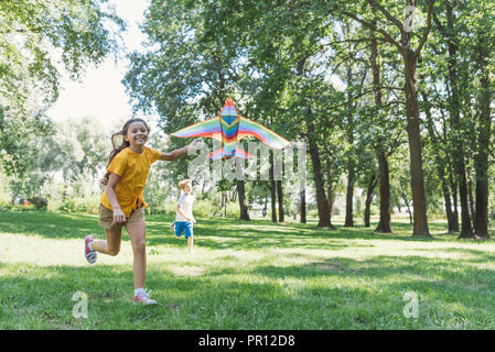 Adorable glückliche Kinder spielen mit bunten Drachen in Park Stockfoto