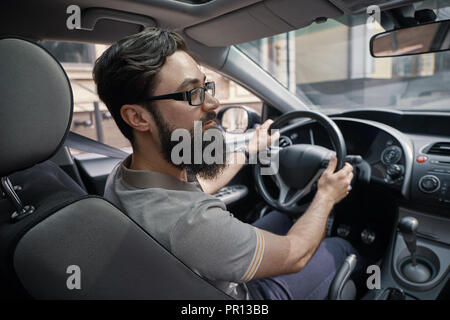 Menschen und Stadt stellt Konzept. Eine positive bärtiger Mann mit seinem Auto fährt durch die Stadt, während die Straße beobachten. Leben jeden Tag einfache Momente Stockfoto