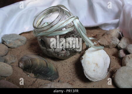 Glas Kristall das Befüllen der kleinen Steine und Muscheln lag auf Sea Sand Souvenir aus Sommer Wochenende am Meer Stockfoto