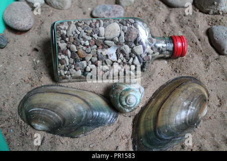 Glas Kristall das Befüllen der kleinen Steine und Muscheln lag auf Sea Sand Souvenir aus Sommer Wochenende am Meer Stockfoto