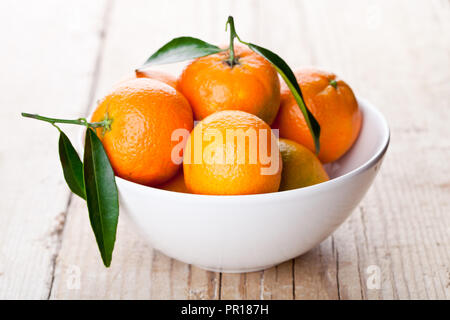 Mandarinen mit Blättern in Schale auf Holztisch Stockfoto