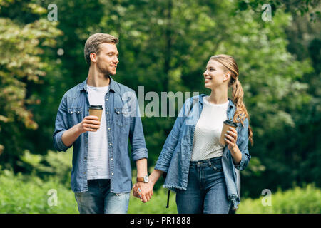 Schöne junge Paar mit Papier Tassen Kaffee zu Fuß durch Park zusammen, und an jedem anderen Suchen Stockfoto