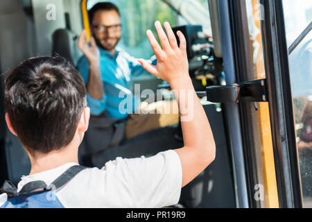 Ansicht der Rückseite des Schülers winken glücklich Busfahrer während der Eingabe von Bus Stockfoto