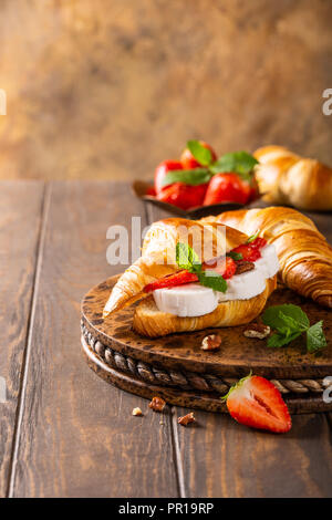 Frisches Sandwich mit Croissant mit Ziegenkäse, Erdbeeren, Honig und Pekannüsse auf Holz Schneidebrett mit kopieren. Stockfoto