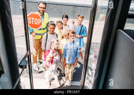 Blick von der Schule Bus an der Gruppe der glückliche Gelehrte mit traffic Guard bei Camera suchen Stockfoto