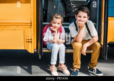 Adorable kleine Wissenschaftler sitzen auf der Treppe der Schule Bus Stockfoto