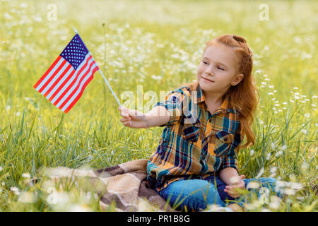 Cute kid mit amerikanischen Fahnenmast ruht auf grünen Gras im Feld Stockfoto