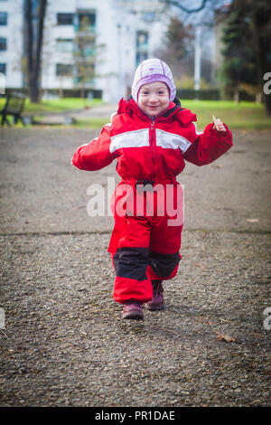 Lustige Kleinkind in Rot winter Jumpsuit läuft gerne in Richtung Kamera Stockfoto