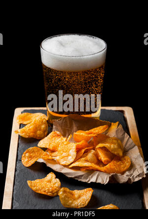 Glas Lagerbier mit Kartoffelchips Snack auf Stein Board auf schwarzem Hintergrund. Stockfoto