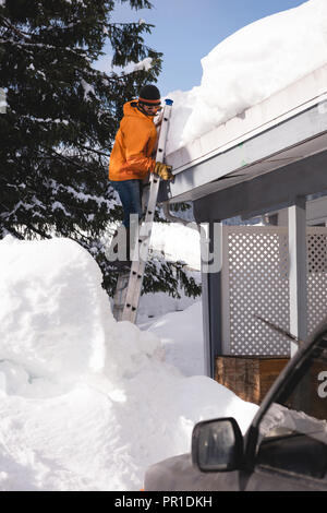 Man Klettern auf einer Leiter zu reinigen Schnee vom Dach seines Geschäftes Stockfoto