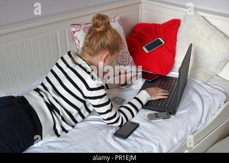 Junge Mädchen (Jugendlicher, Kind, Frau) sich auf weiße Couch benötigten Laptop und eine der wenigen Smartphones gleichzeitig, in ihr Zimmer. Stockfoto