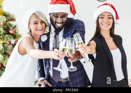 Lächelnd multikulturellen Geschäftsleute in santa Hüte klirren mit Gläser Champagner in Office Stockfoto