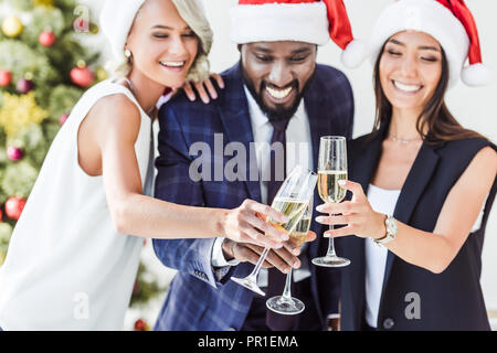 Lächelnd multiethnischen Geschäftsleute in santa Hüte klirren mit Gläser Champagner in Office Stockfoto