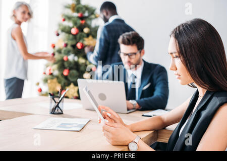 Asiatische Geschäftsfrau und Kollegen schmücken Weihnachtsbaum im Büro Stockfoto