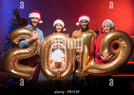 Lächelnd multiethnischen Geschäftsleute in santa Hüte Holding 2019 Ballons am neuen Jahr Corporate Partei Stockfoto