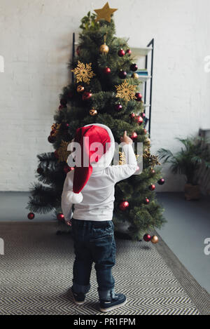 Rückansicht des männlichen Kindes in Santa hat an Weihnachten Baum zeigen Stockfoto