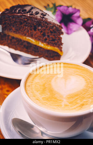 Tasse Cappuccino mit leckeres Stück Sachertorte auf dem hölzernen Tisch Stockfoto