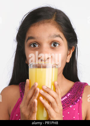 Junge indische Mädchen trinken Orangensaft. Schuß GEGEN EINEN EINFACHEN HINTERGRUND Stockfoto