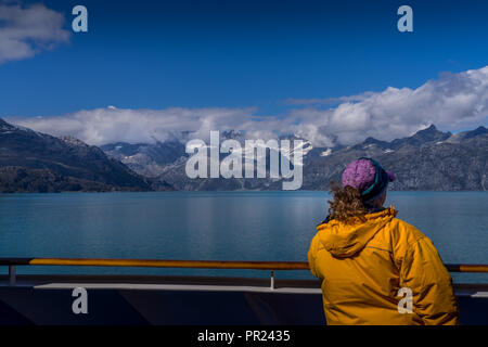 Glacier Bay, Alaska USA - 17.August 2018. Eine Frau mit einem schönen Blick auf Glacier Bay mit Schnee bedeckte Berge, blauer Himmel und weiße Wolken aus. Stockfoto